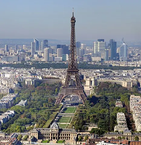 Vue aérienne de la Tour Eiffel à Paris, en France, sur fond de gratte-ciel et de paysage urbain modernes. Le célèbre monument se dresse au milieu des bâtiments environnants et des jardins verdoyants, capturant le mélange d'architecture historique et contemporaine : une scène parfaite pour tout Chasseur d'appartement Paris 7.